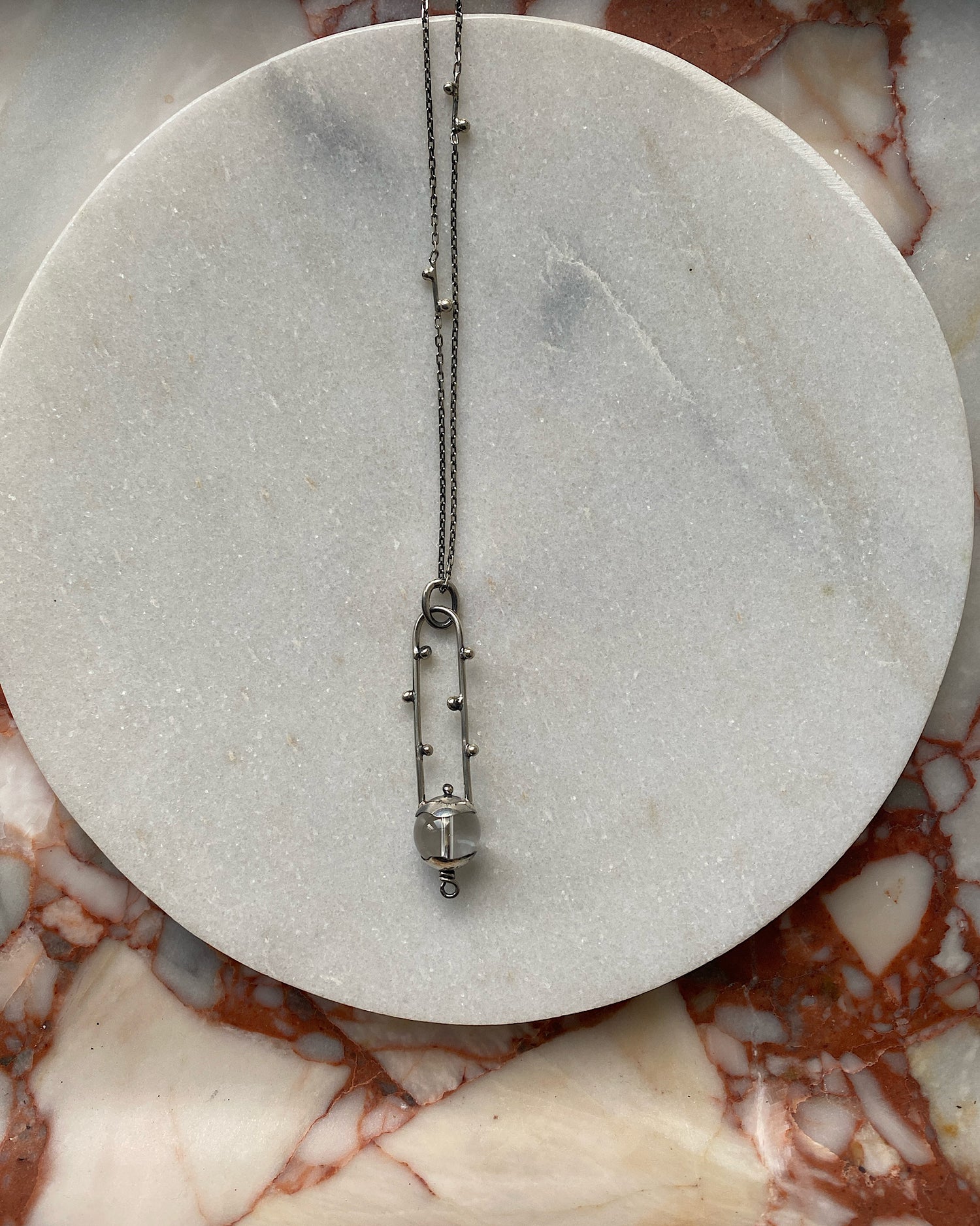 A sterling silver pendant style necklace sits on a marble tray