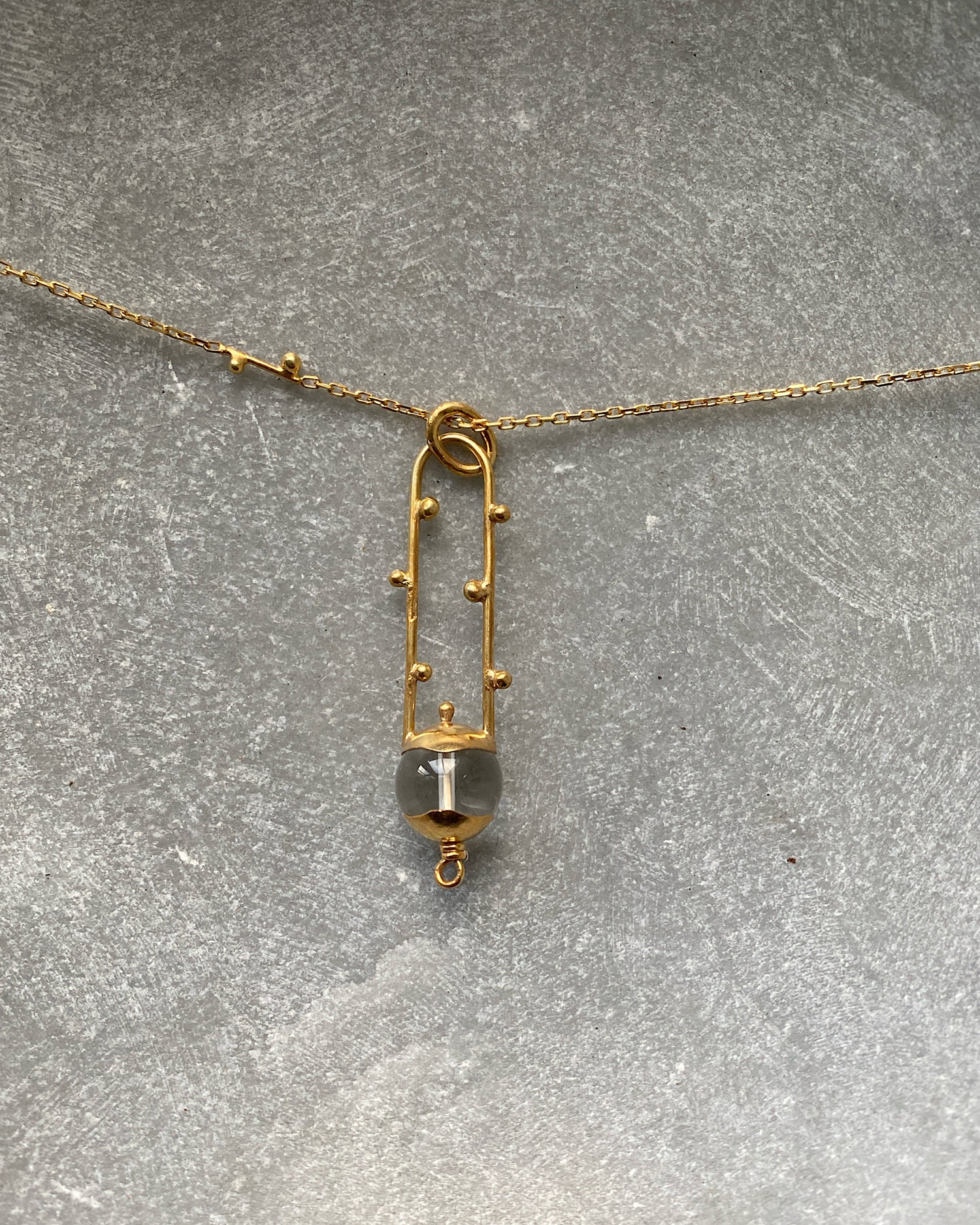 An open style oval pendant with a clear crystal sits on a gold chain