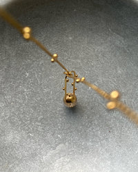 A gold and clear crystal oval pendant sits on a delicate gold chain