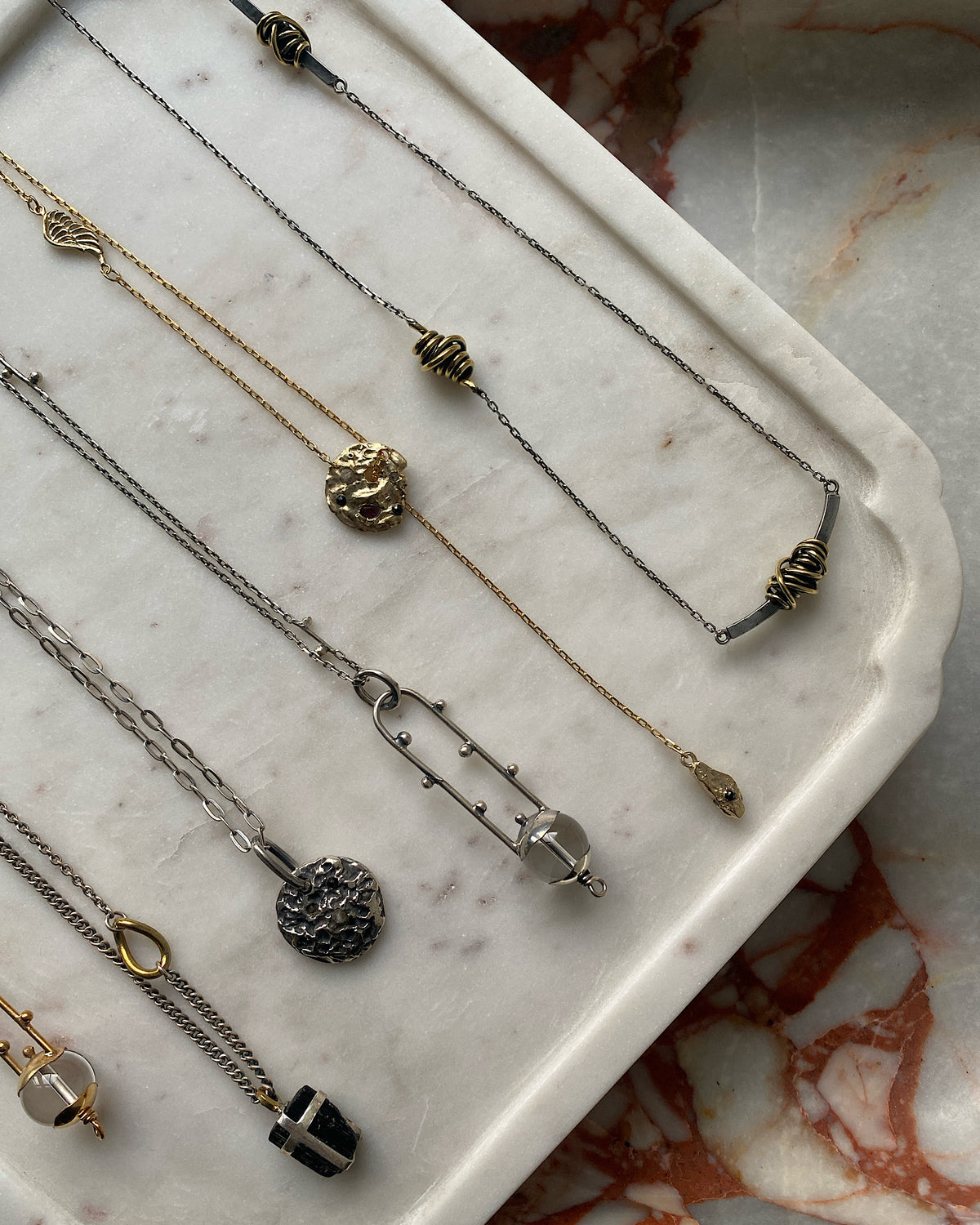 A series of silver johnny ramli necklaces sit on a marble tray