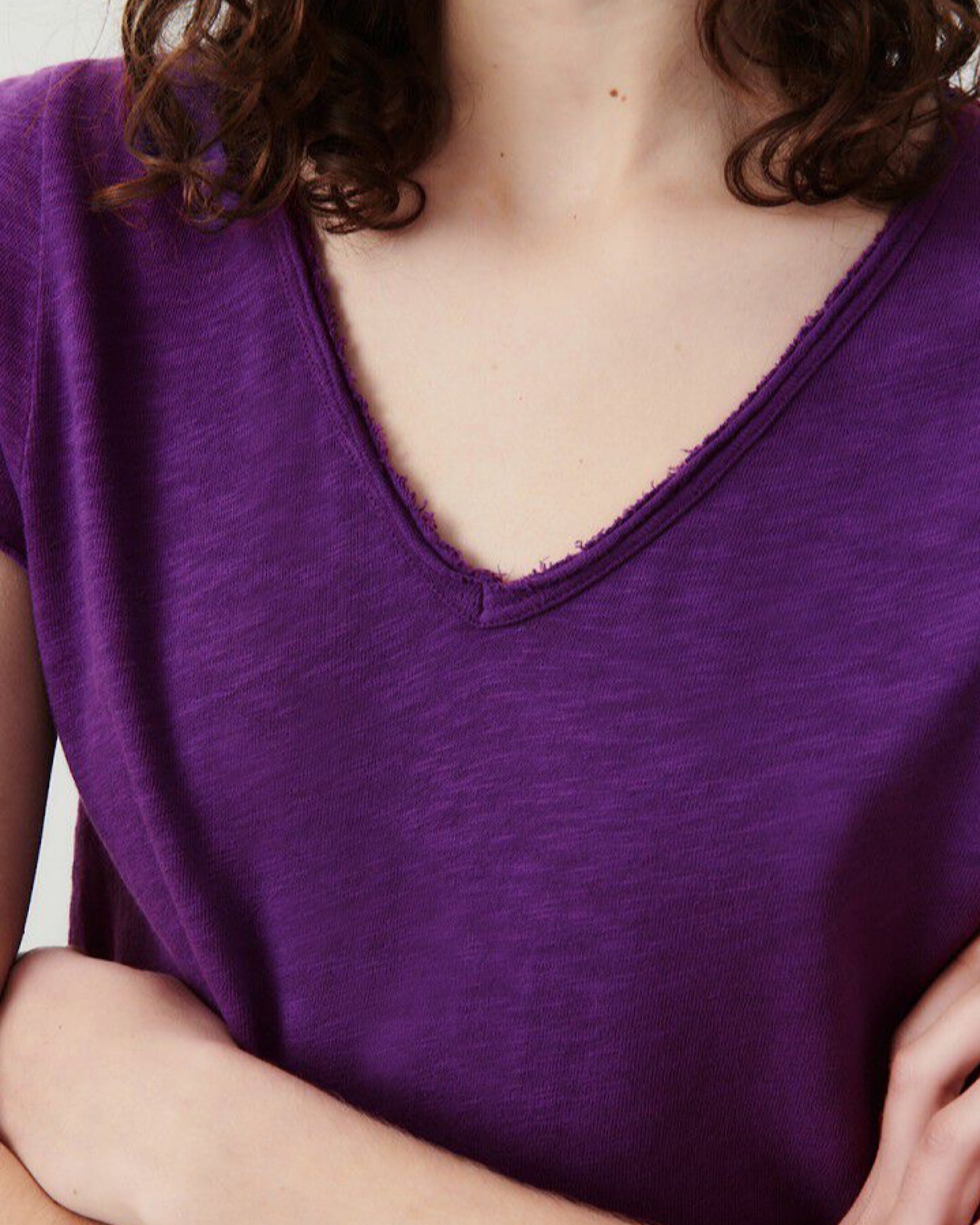 Model wears a vibrant purple v neck t-shirt from American Vintage with a raw edge finish