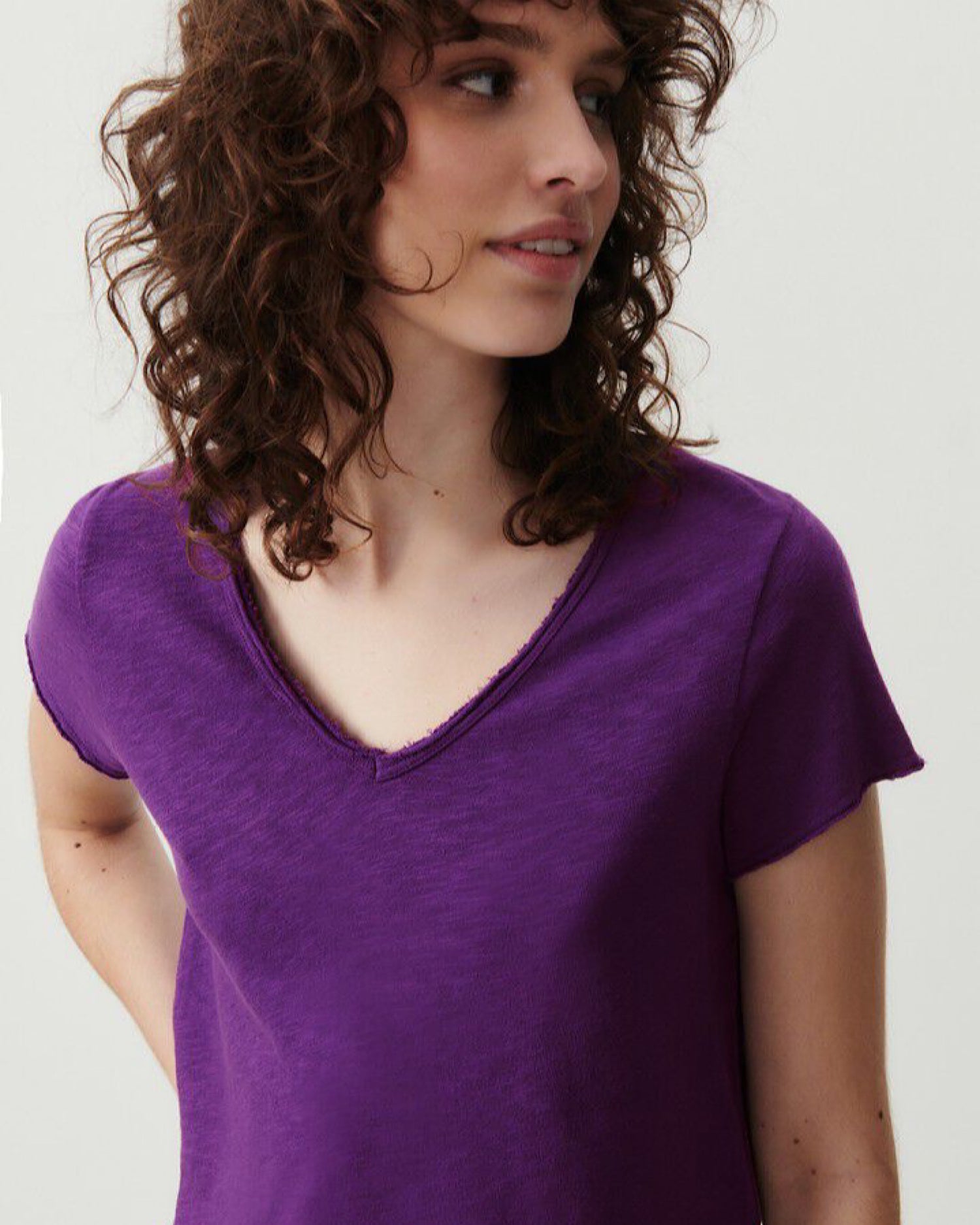 Model wears a vibrant purple v neck t-shirt from American Vintage with a raw edge finish