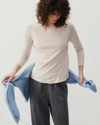 model wears a mastic coloured boat neck long sleeve t-shirt from American Vintage with grey track pants and a blue sweater