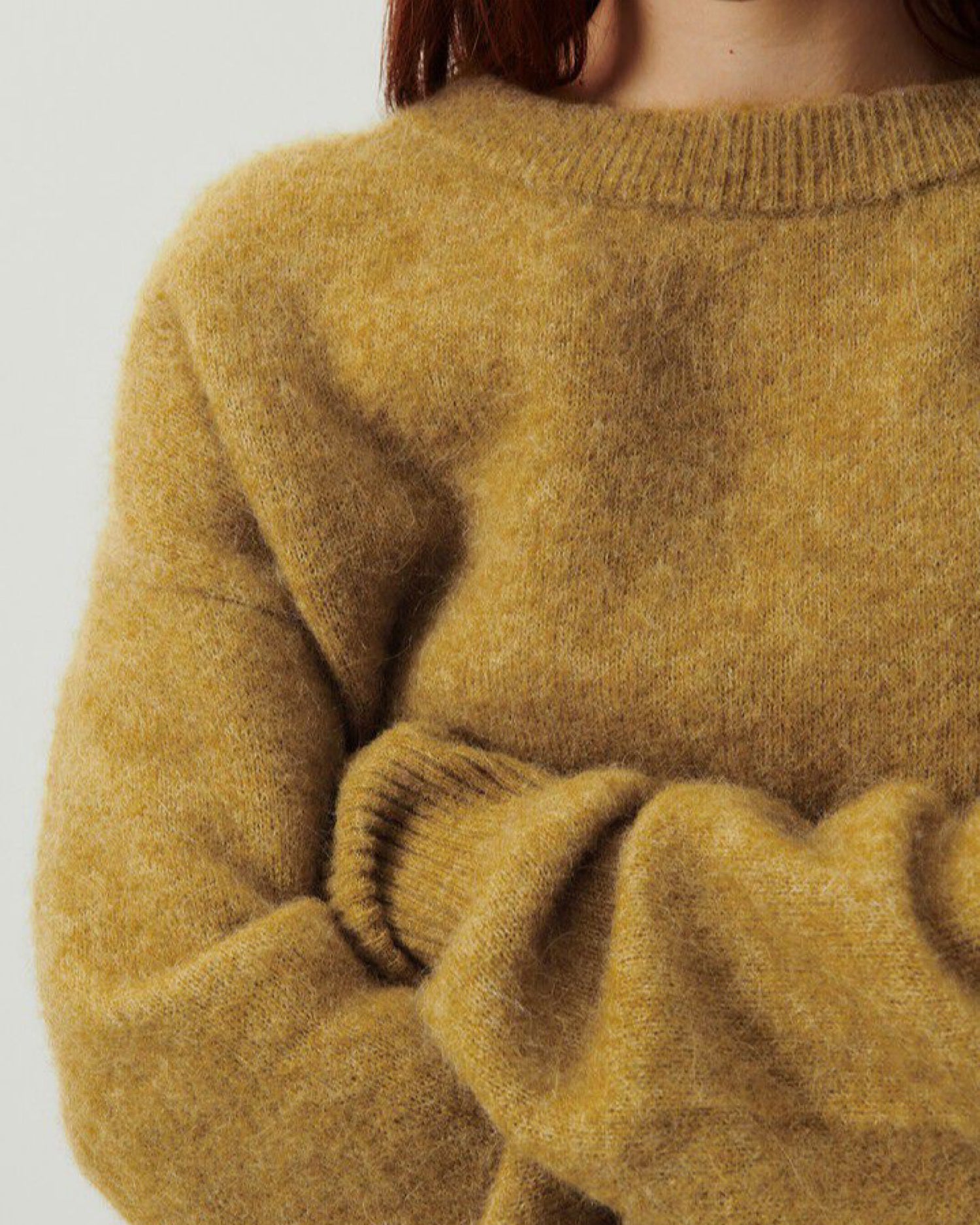 a close up detail of a warm toned olive green sweater on a model with a ribbed neckline and cuffs