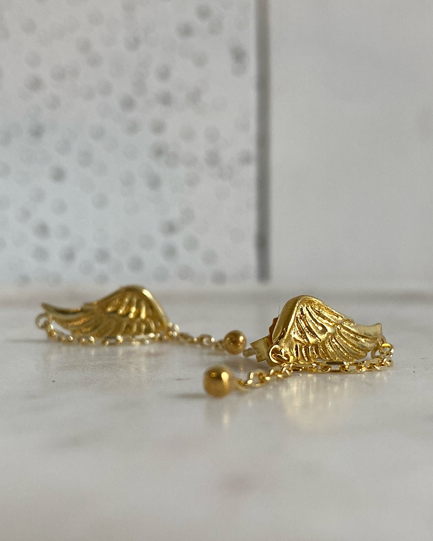 small gold wing earrings with a chain sit on marble