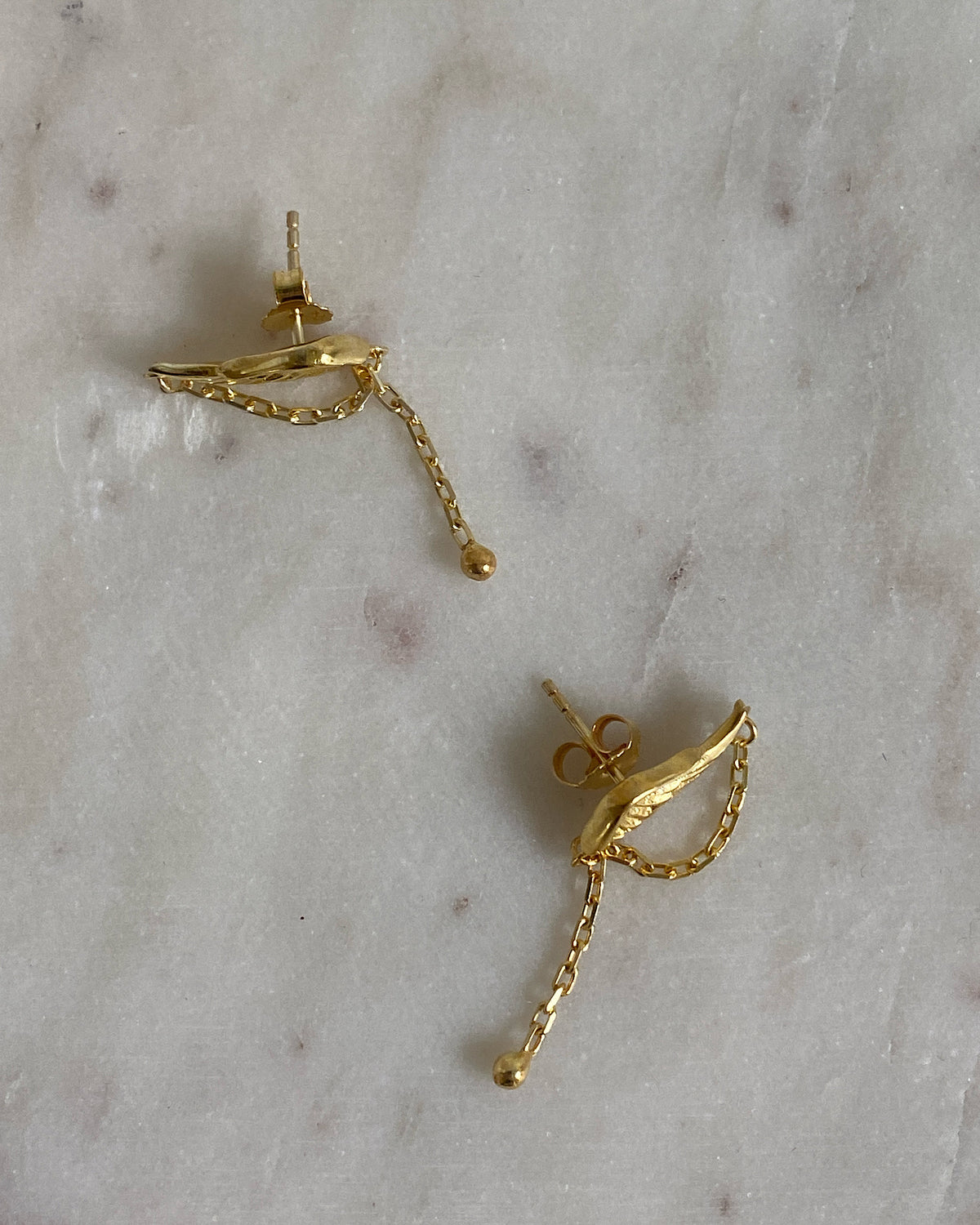 small gold earrings sit on a marble background