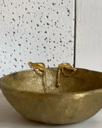 small gold wing earrings sit in a gold bowl