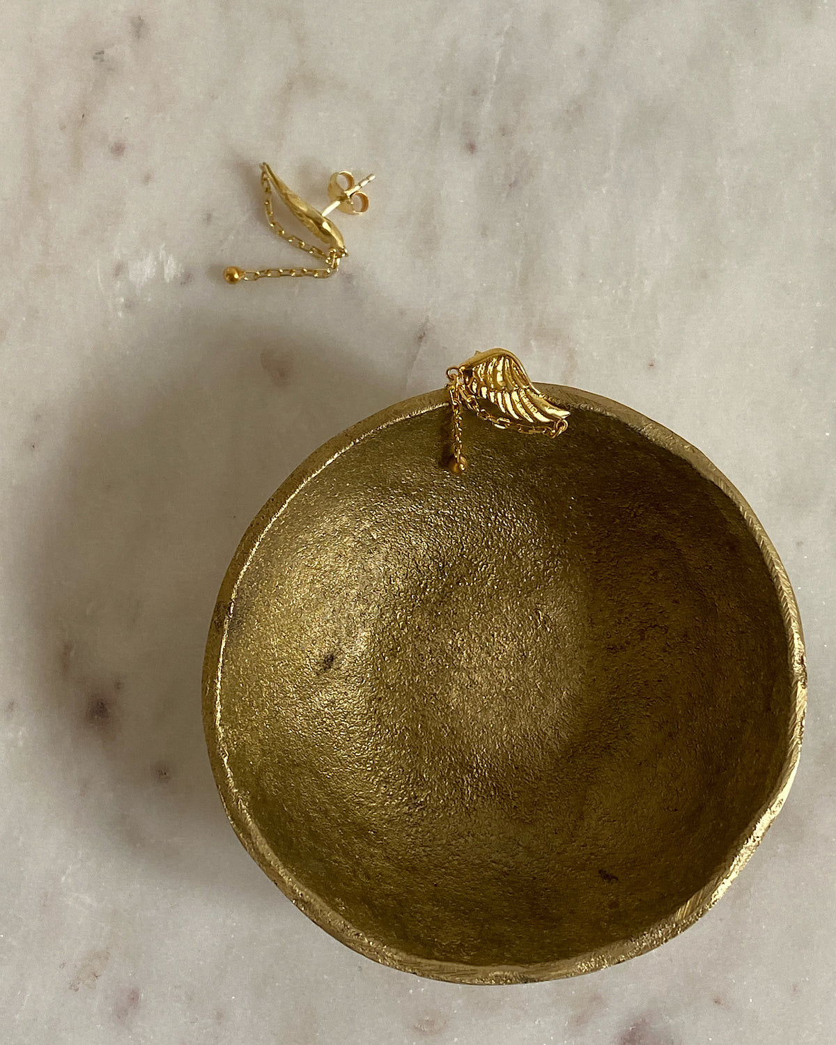 small gold earrings sit in a gold bowl