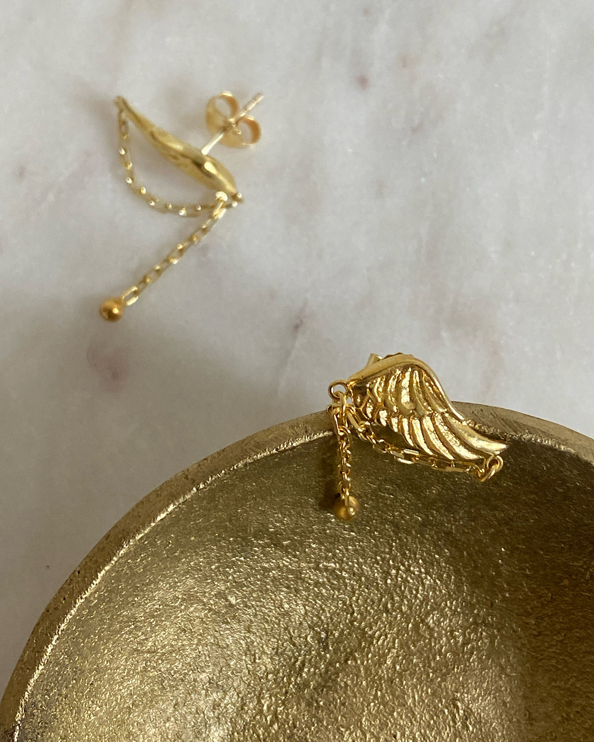 small gold wing earrings in a gold bowl