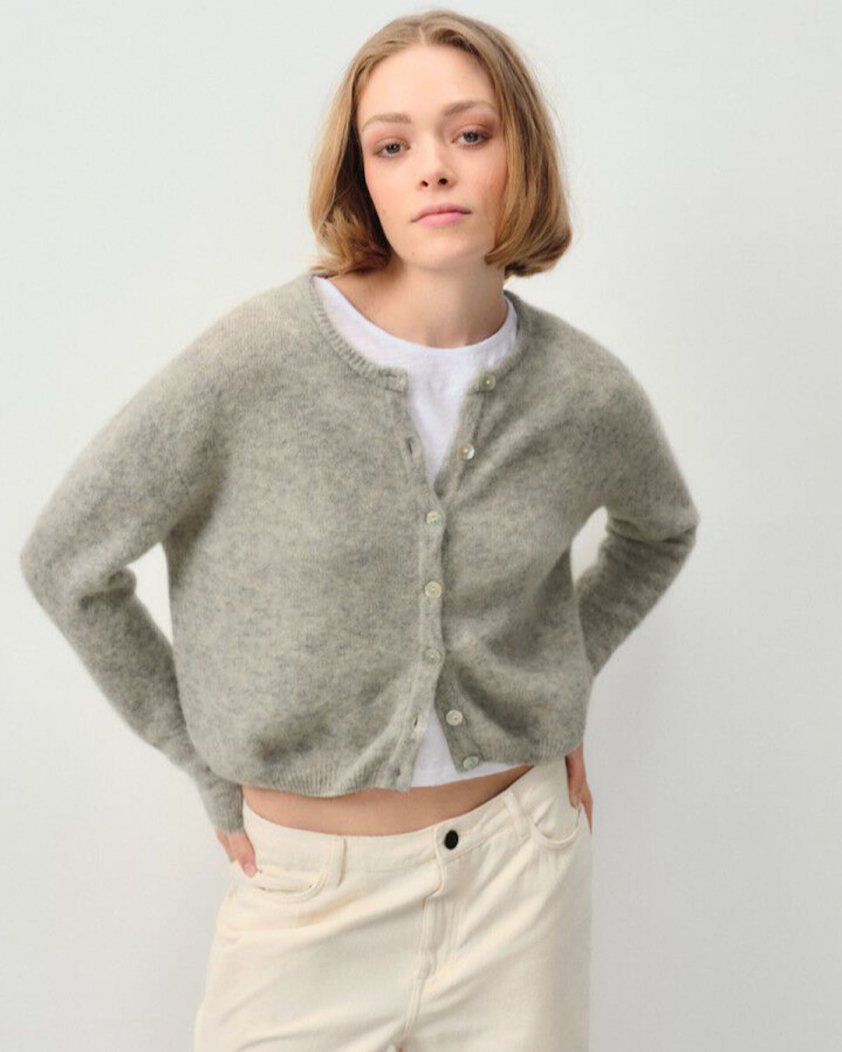 Model wears a grey cardigan and cream jeans