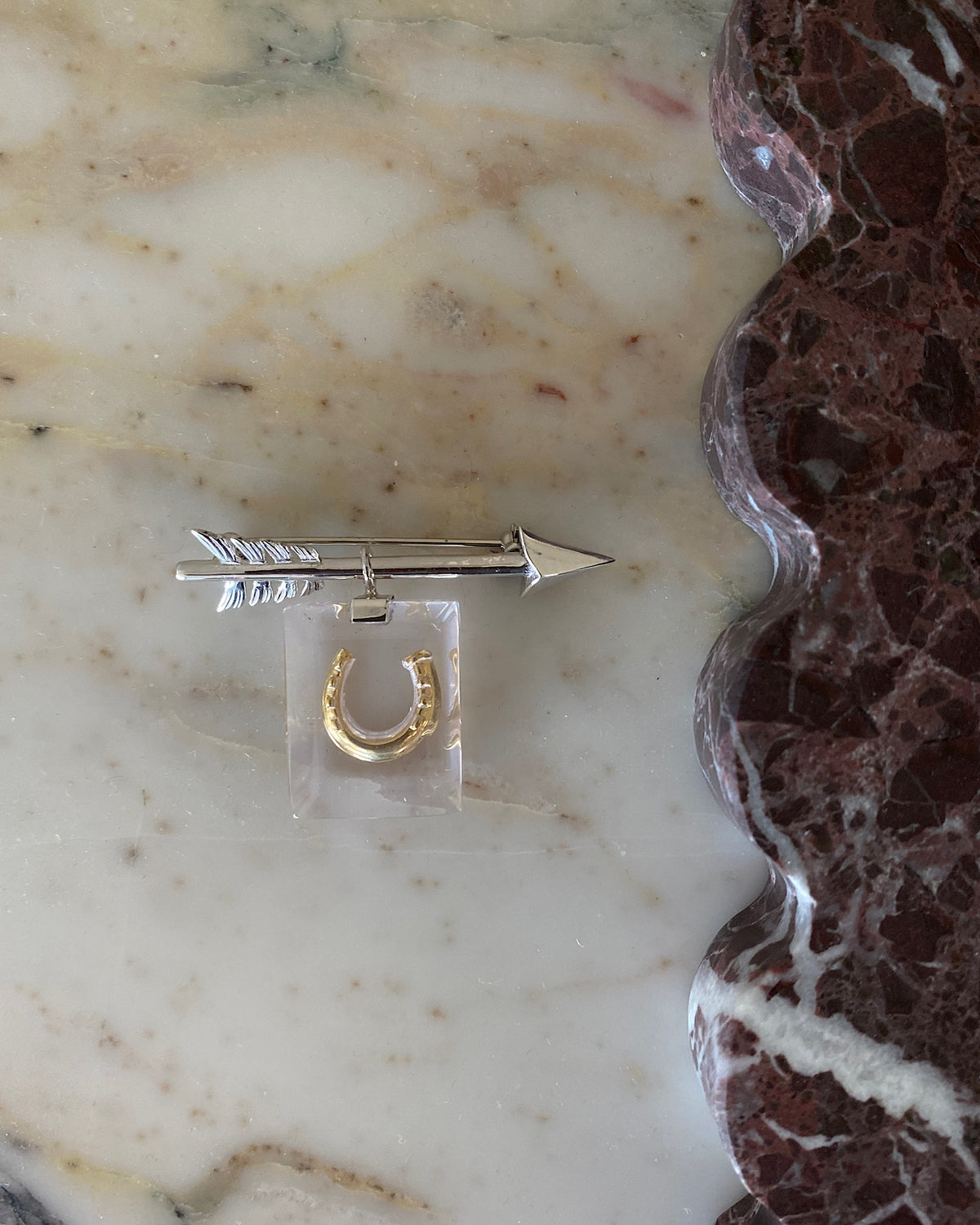 A small silver arrow brooch has a resin charm attached with a gold horseshoe in it