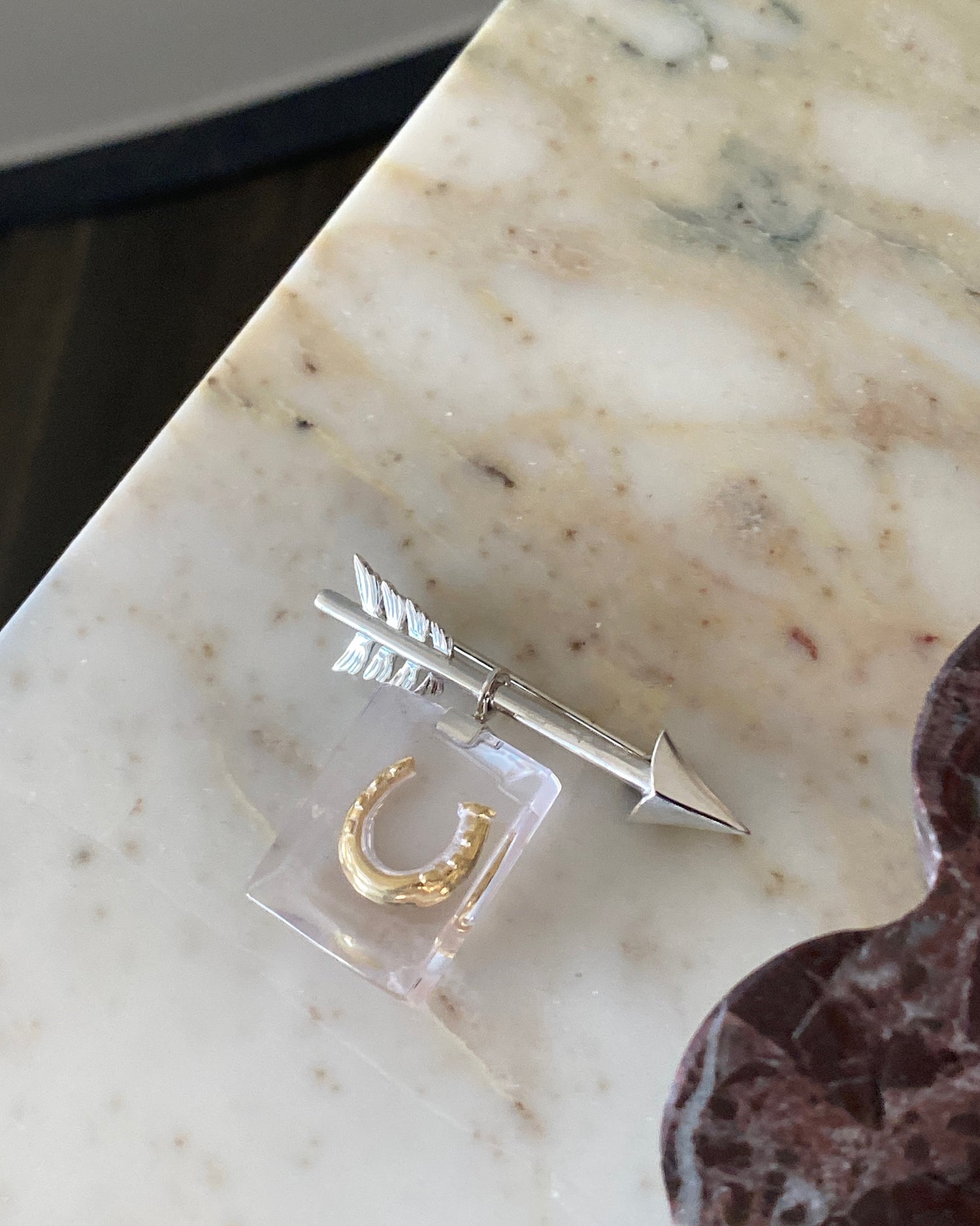 A small silver arrow brooch has a resin charm attached with a gold horseshoe in it