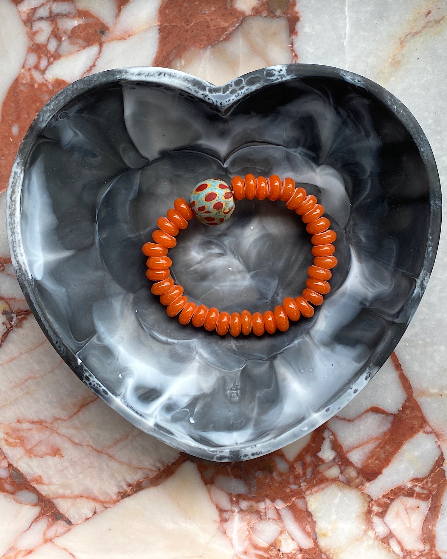 orange beaded bracelet with a central light blue mottled feature bead in a heart bowl