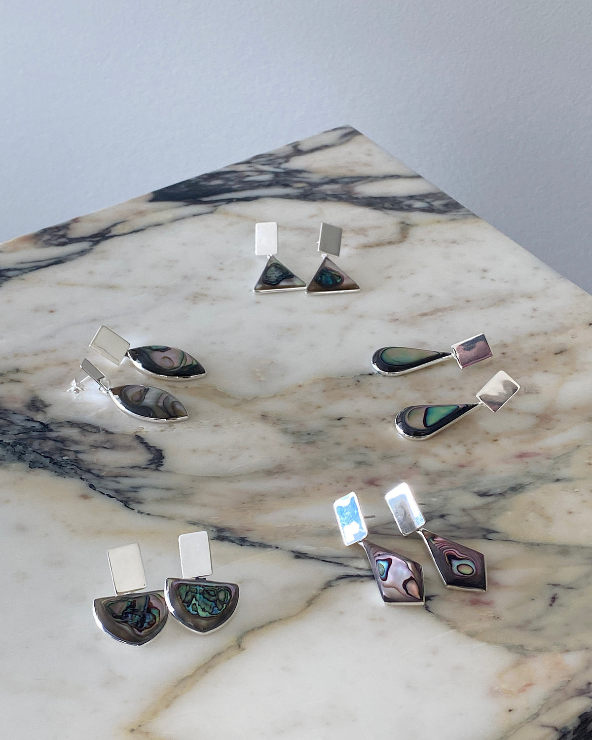 a selection of abalone and silver earrings sit on a marble angular background