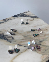 a selection of abalone and silver earrings sit on a marble angular background