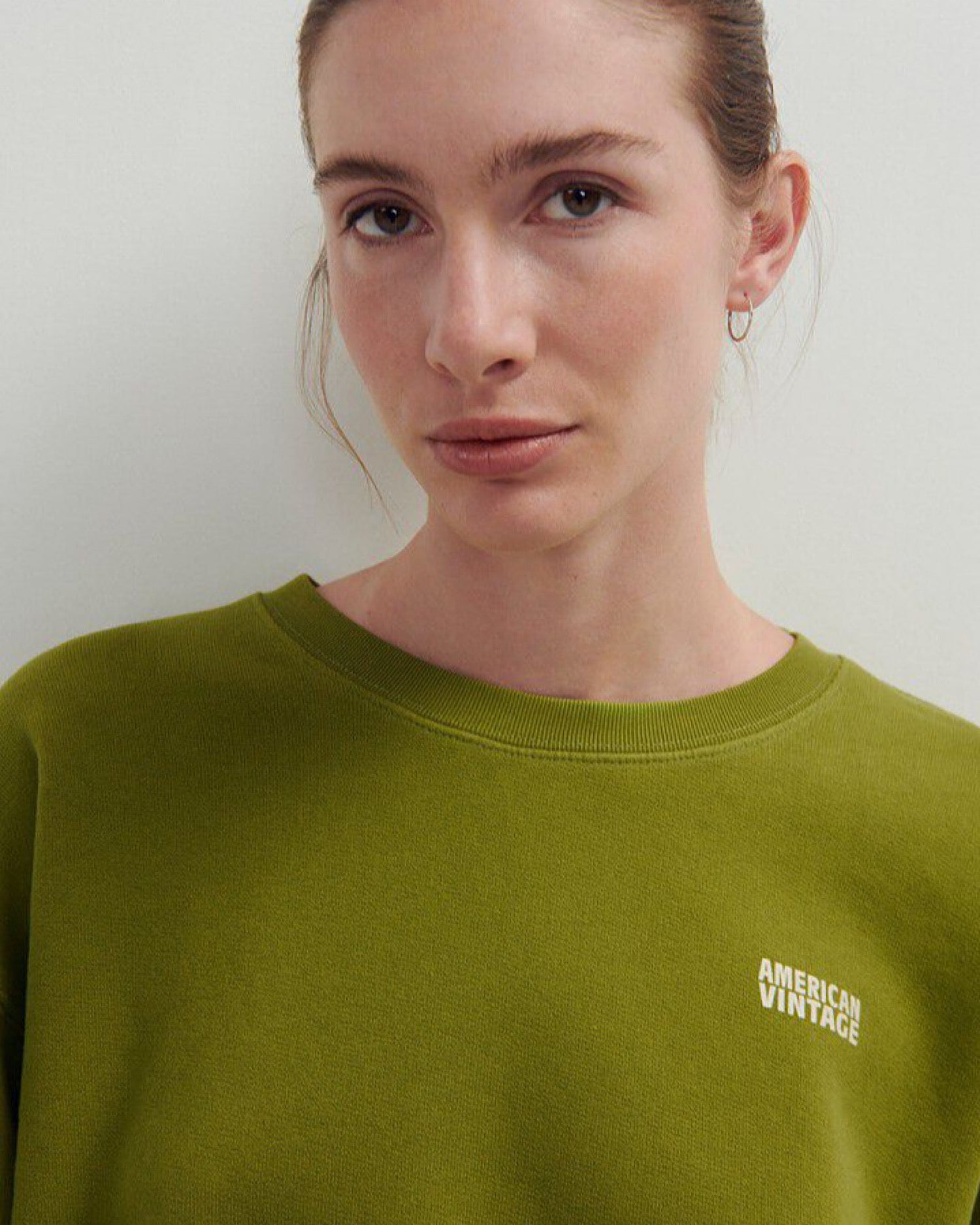 a pea green cropped fleece round neck sweater with a white logo on a model