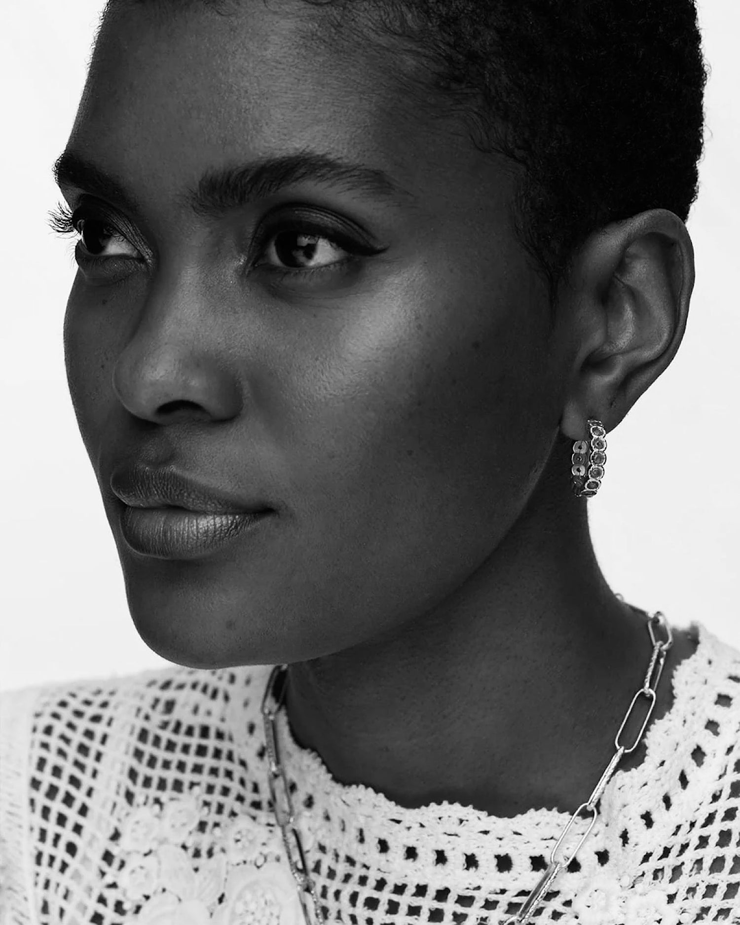 model in a white lace top wears a hoop earring with stones