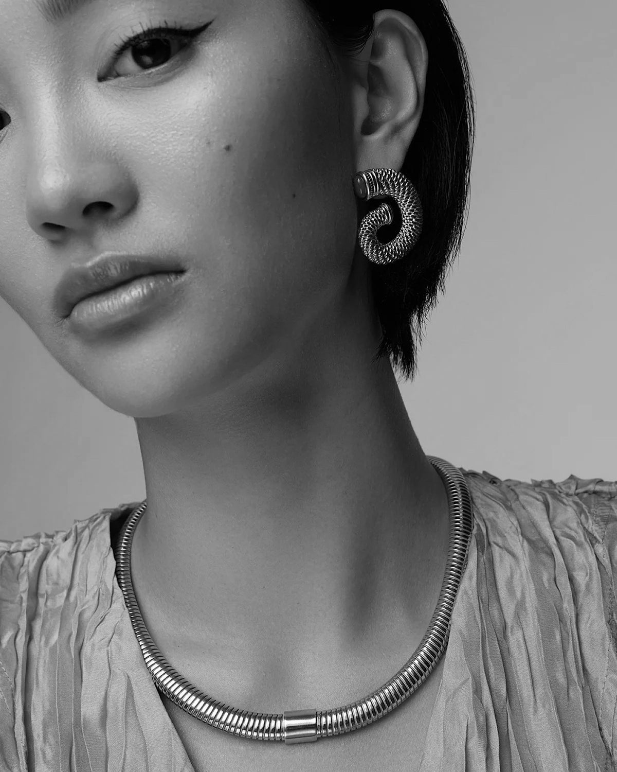 a model wears a wide snake chain necklace and swirl earrings