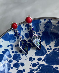 red stud earrings with a blue charm dangling off them sit in a blue mottled bowl