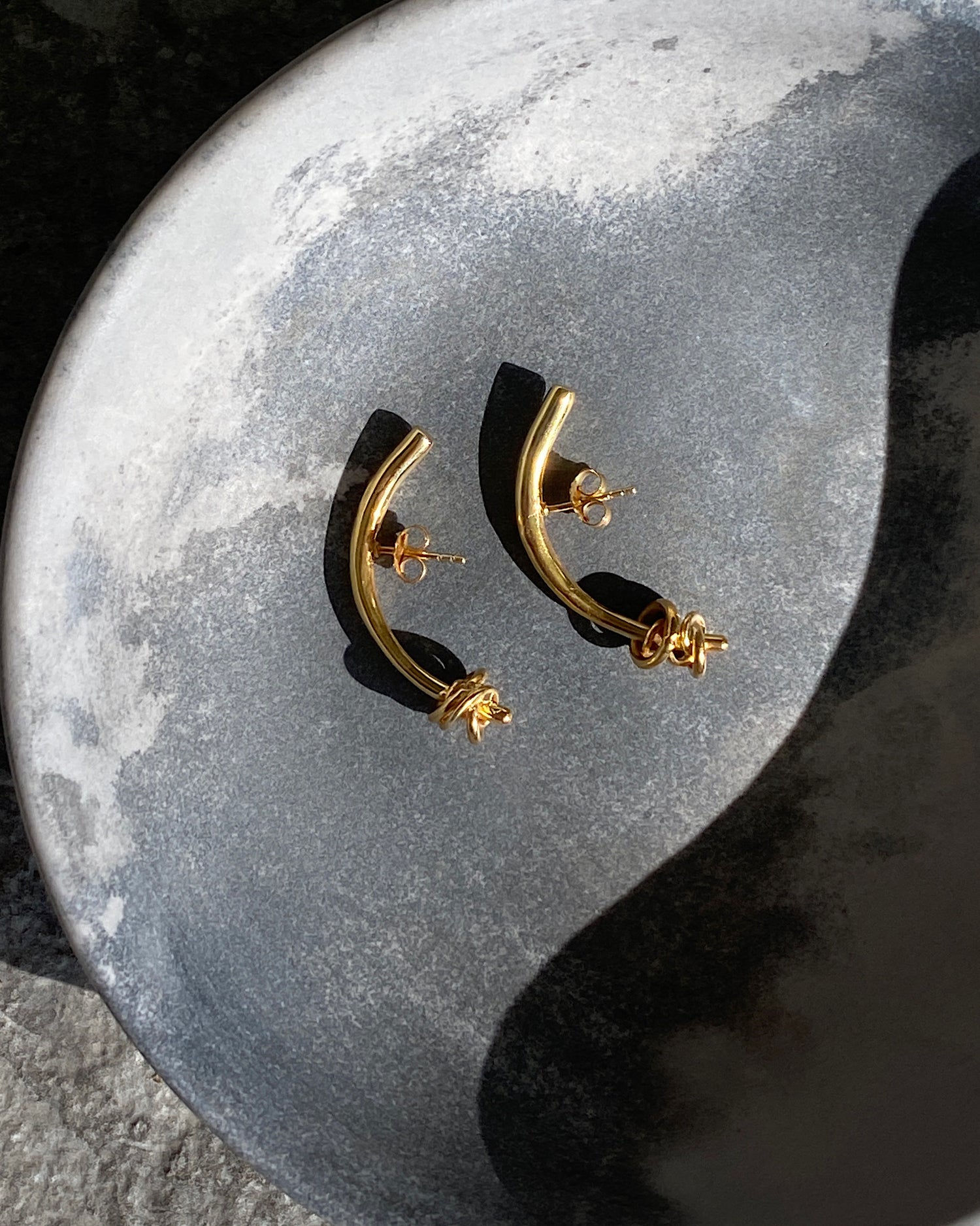 Gold bar curved earrings with ring detail sit in a bowl