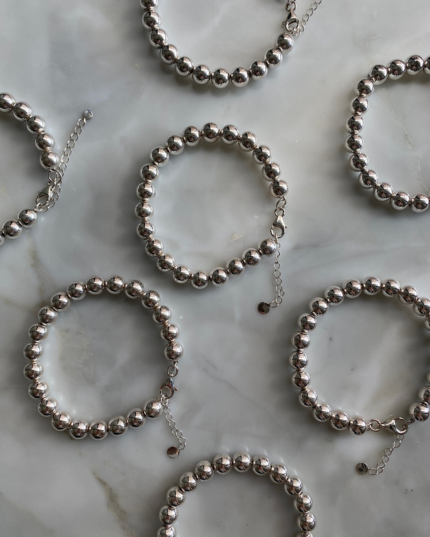 a series of silver ball bracelets with extender chains all the same size against marble