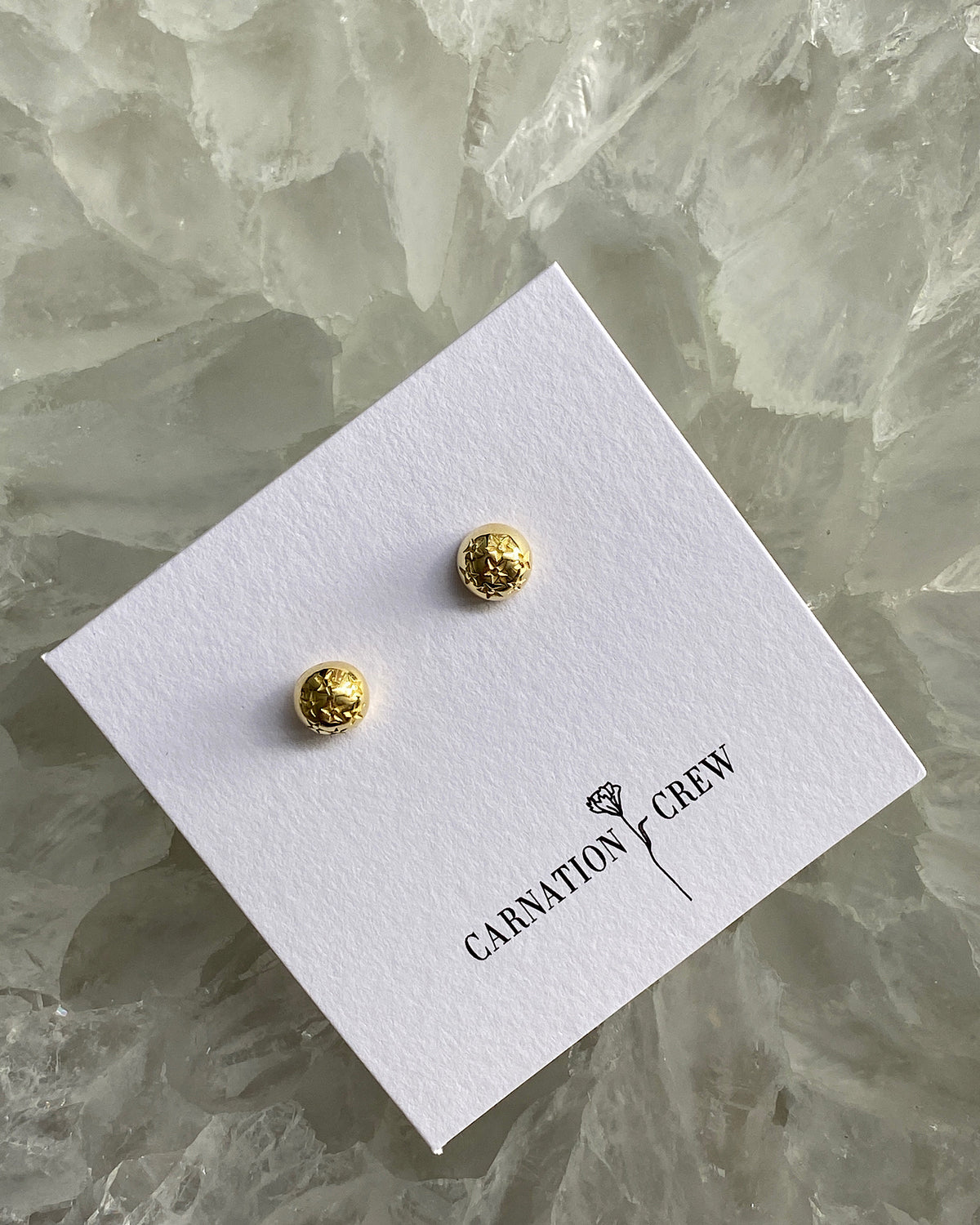 very small gold star stamped dome stud earrings sit ion their display card