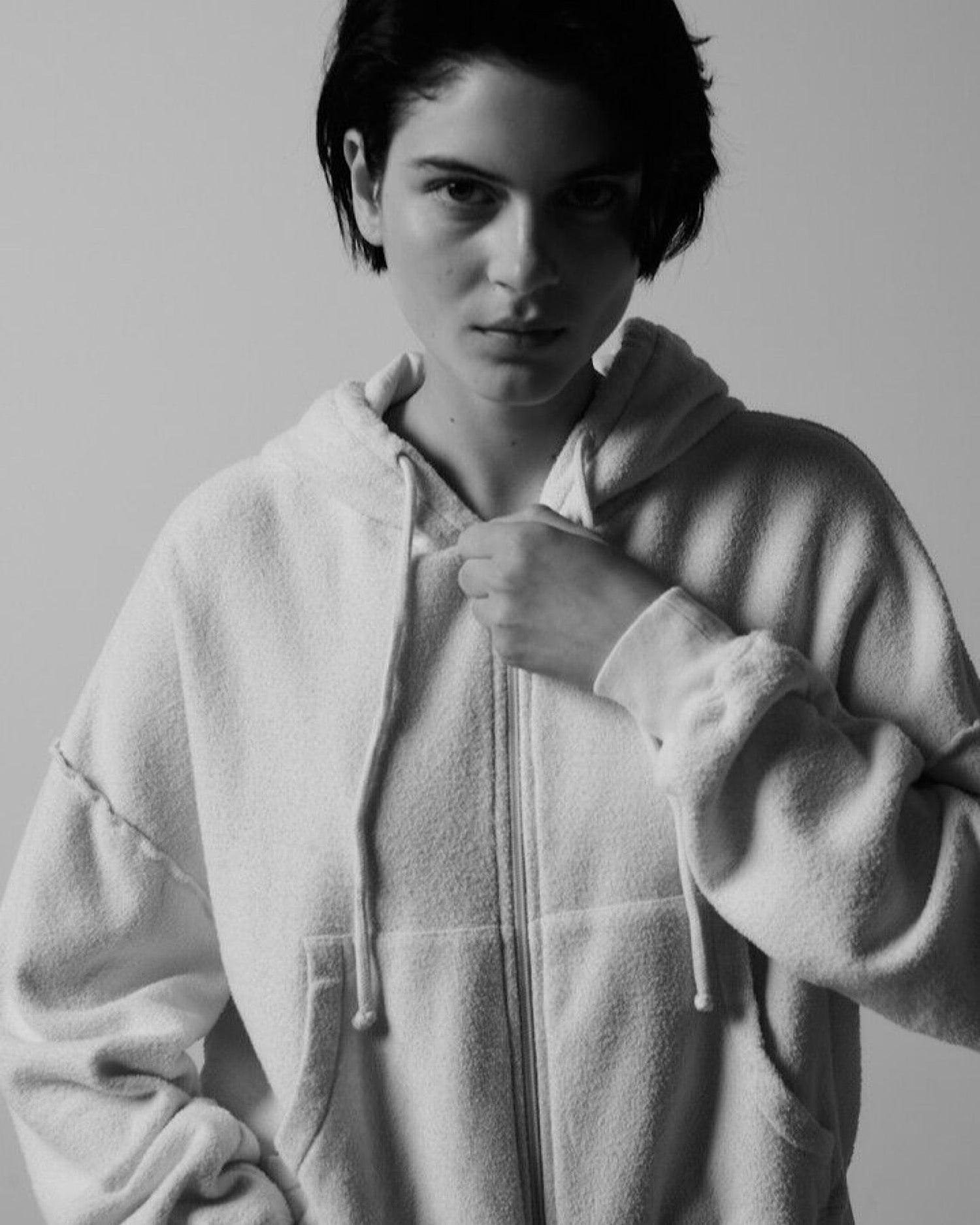 Model wears a boucle style hoodie with zip up front, side pocket and hood pulls