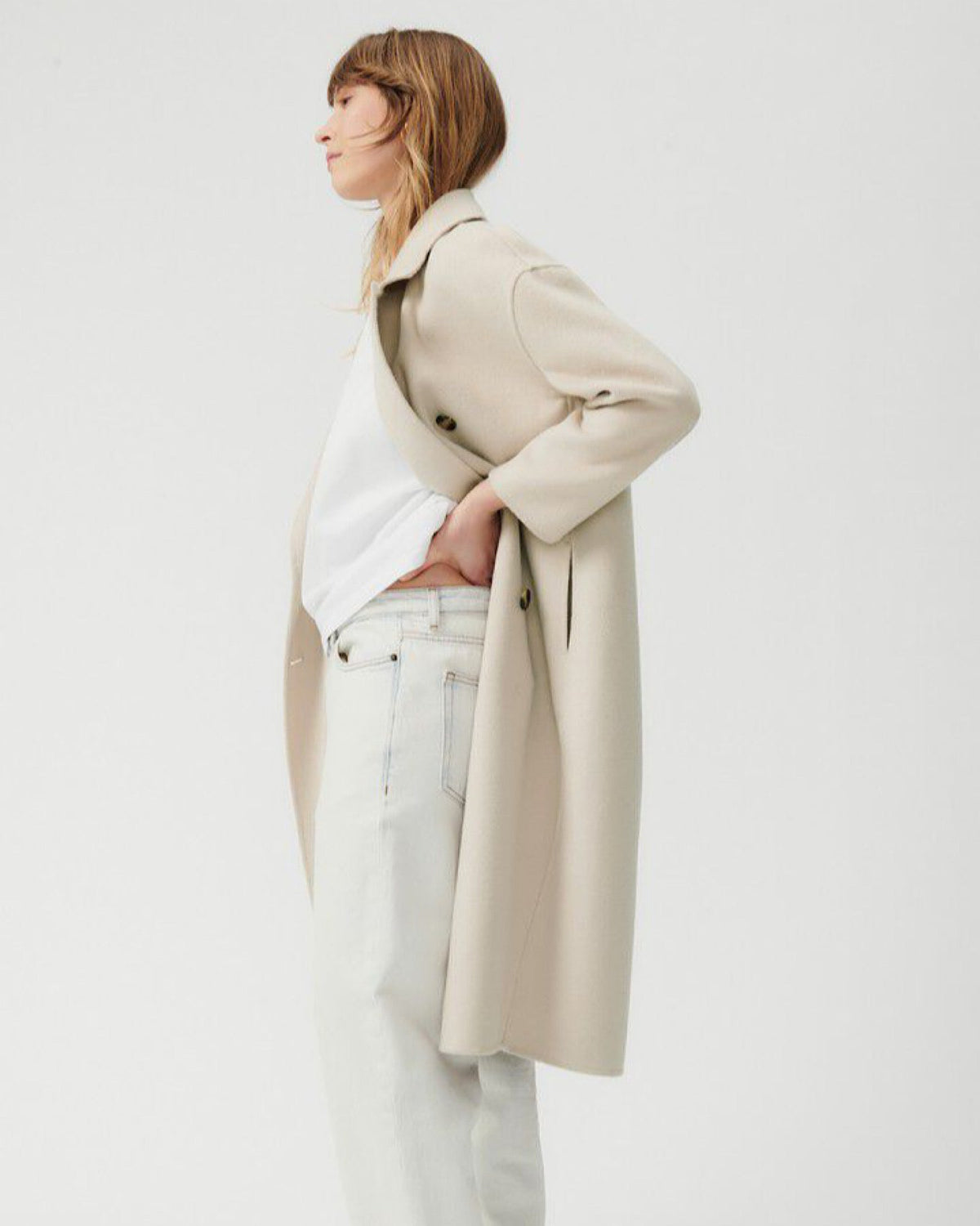 a long light taupe double breasted coat with round two toned buttons and wide lapels