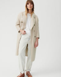 a long light taupe double breasted coat with round two toned buttons and wide lapels