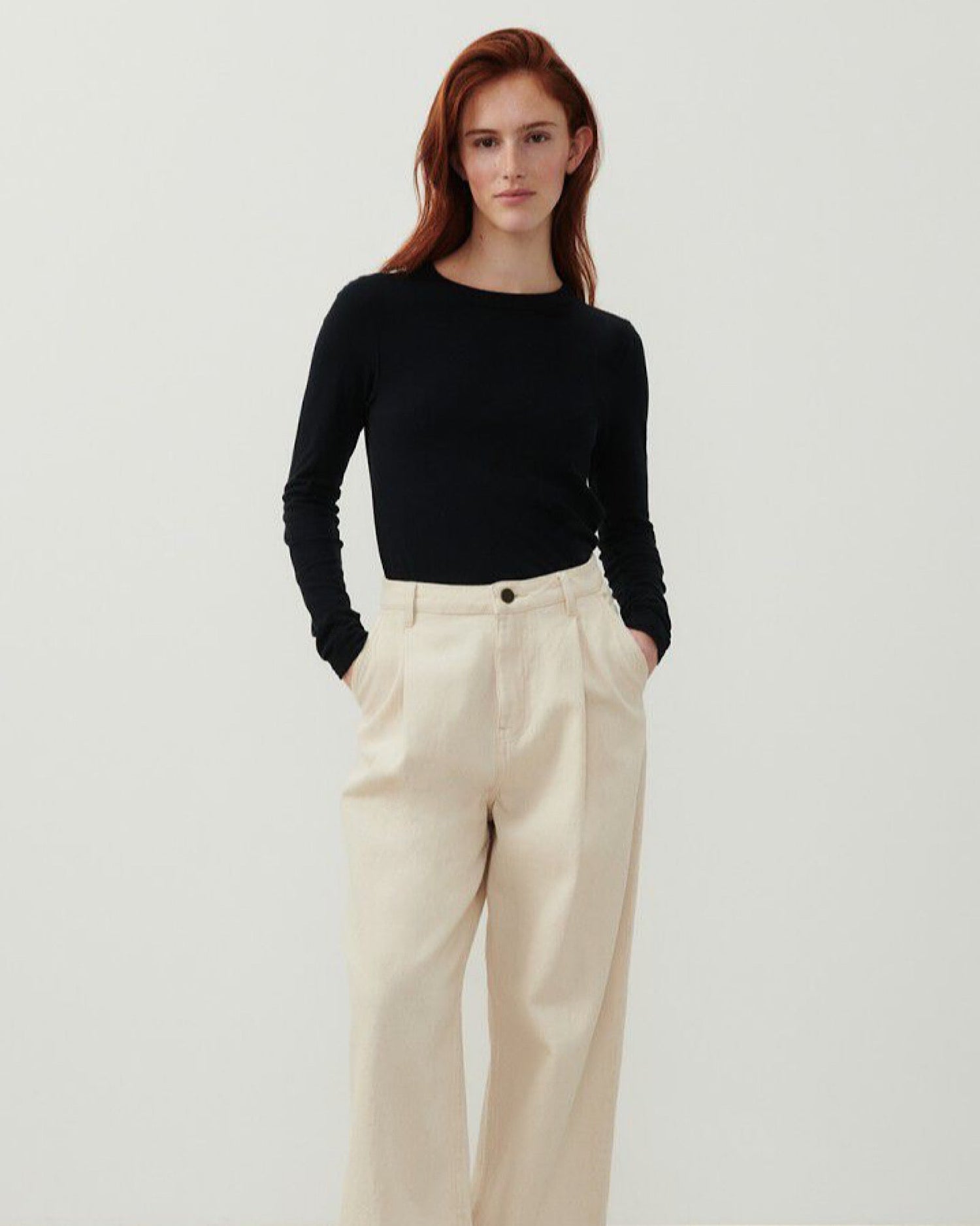 a model wearsa long sleeve black T-Shirt with a high round neck and cream pants