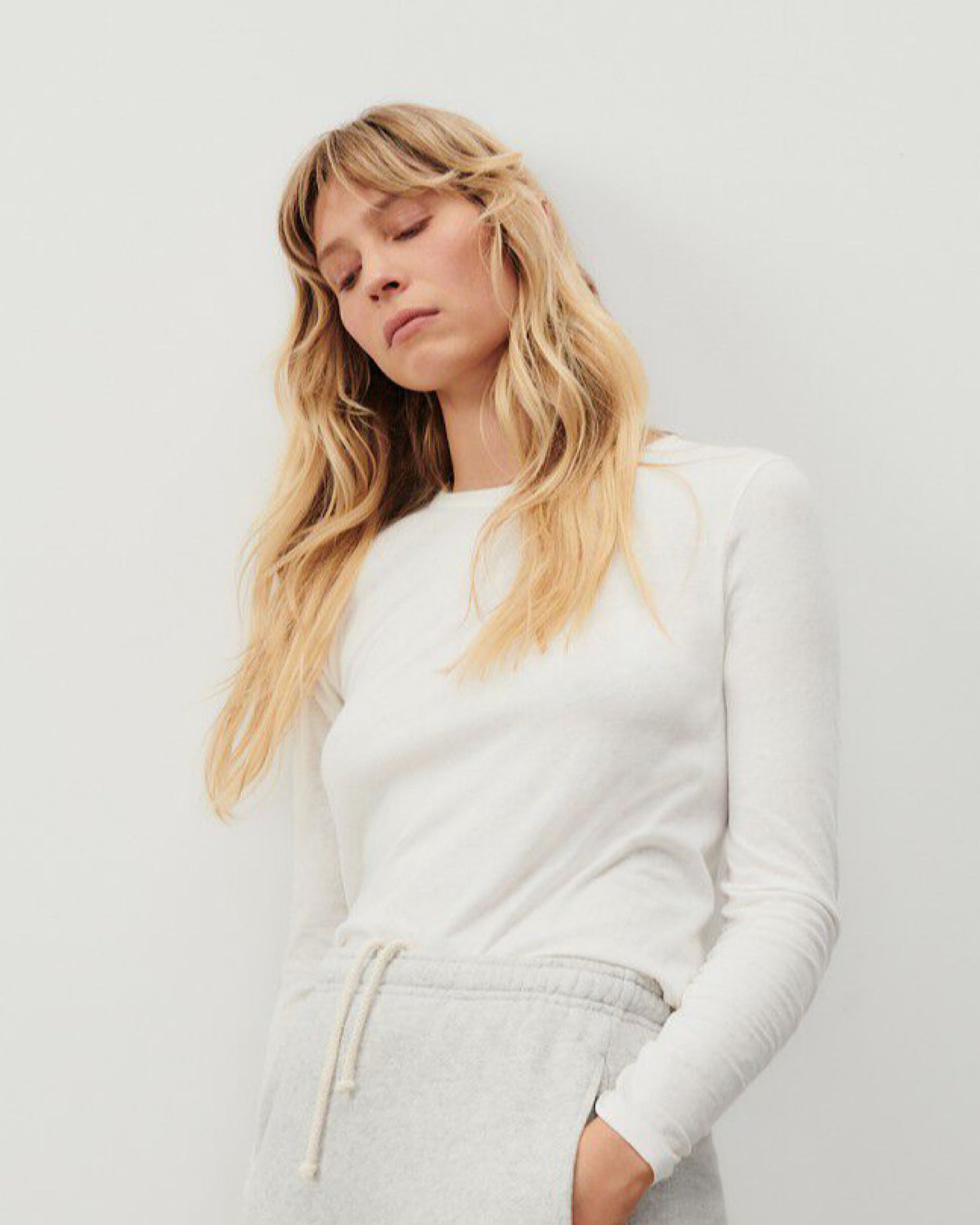 model wears a long sleeve round neck white t-shirt with grey pants