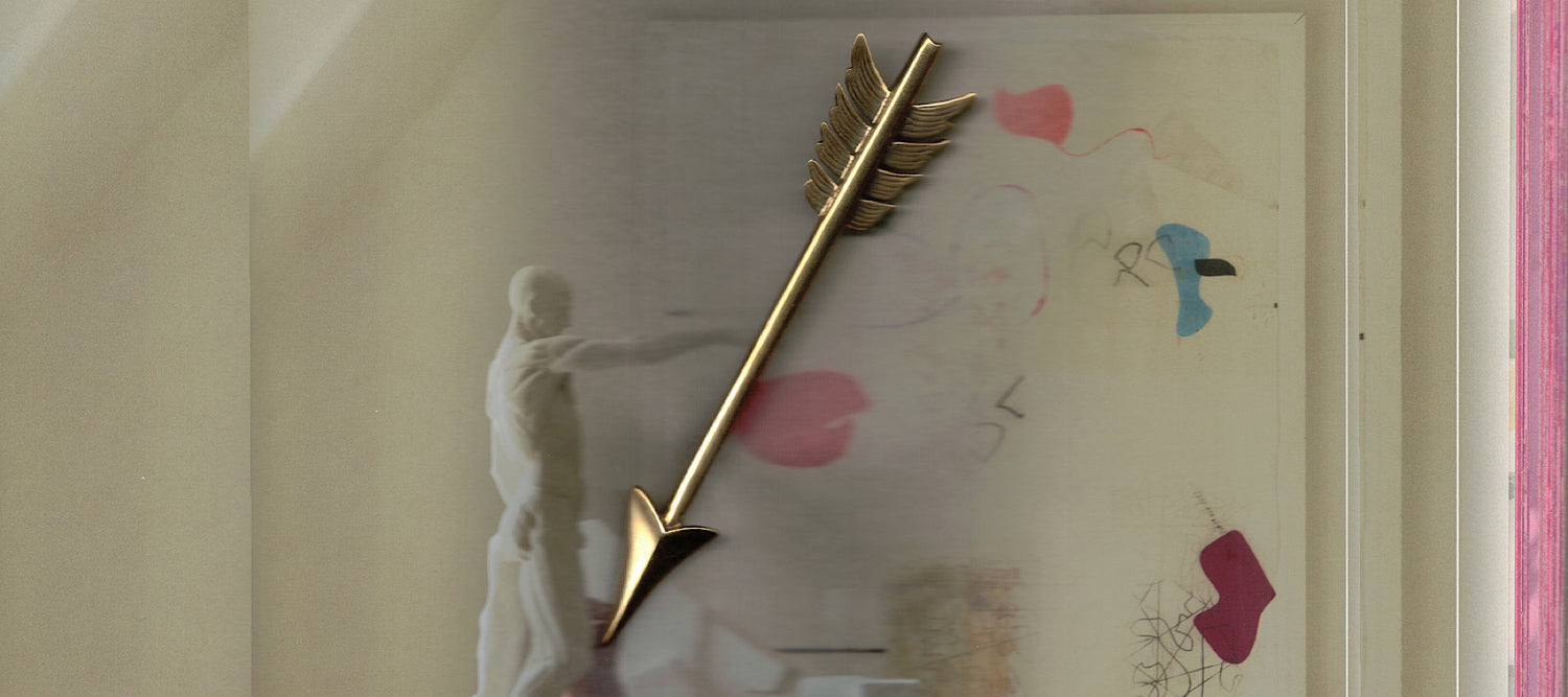 a gold arrow brooch sits on a colourful background