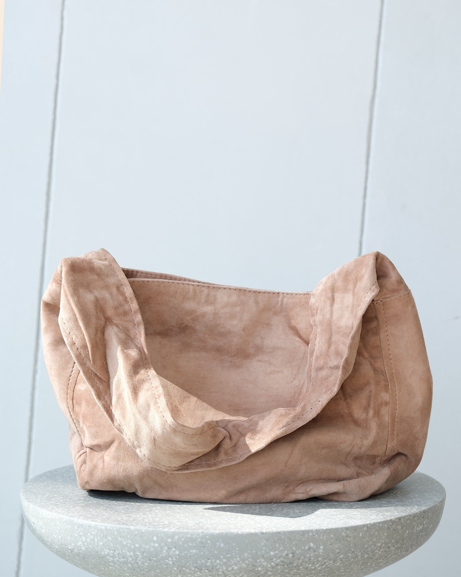 a taupe slouchy suede bag sits on a stool