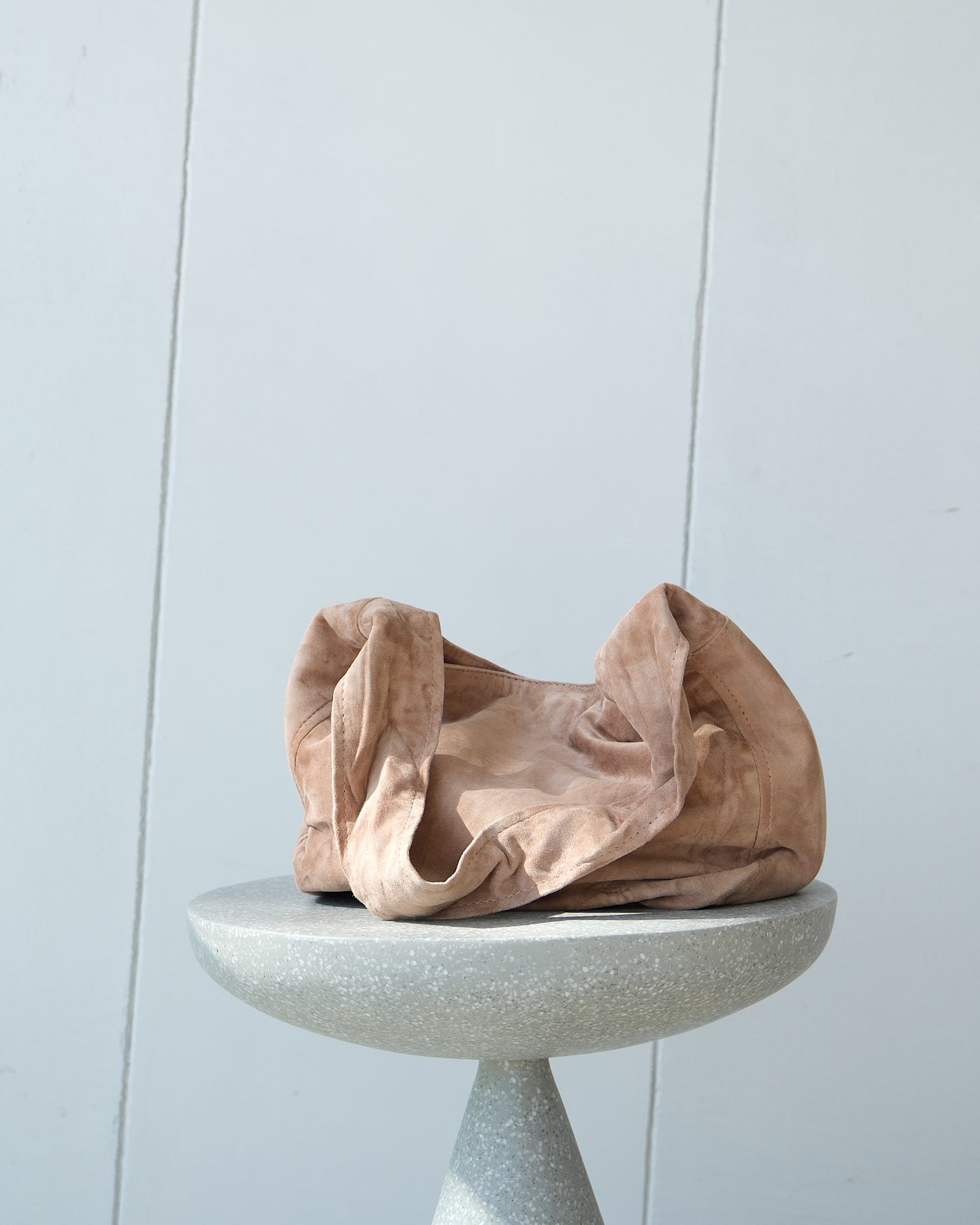 a taupe slouchy suede bag sits on a stool