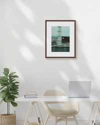 Framed artwork on a white wall above a desk with a plant and laptop.
