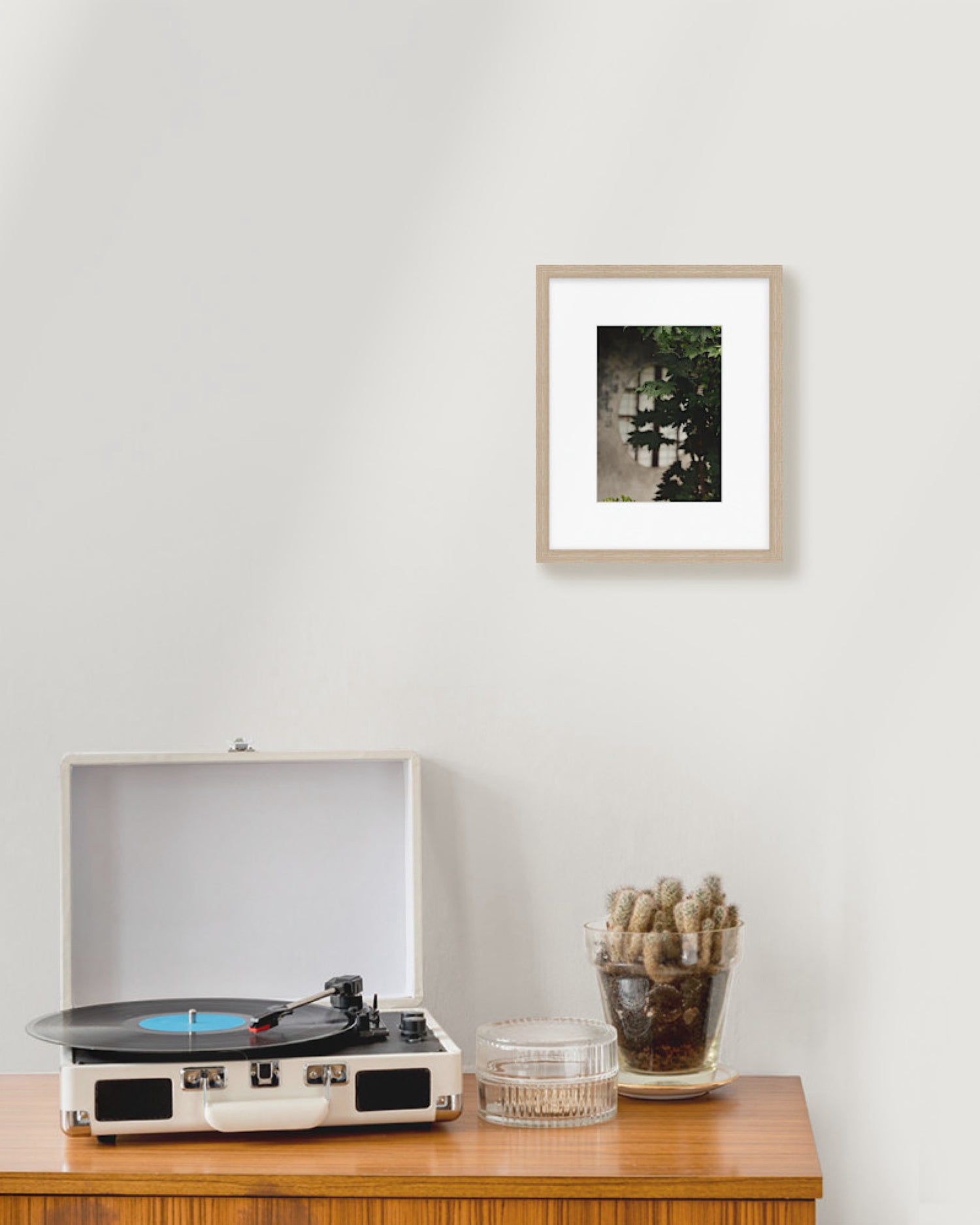 Record player on a wooden table with a framed picture on the wall.
