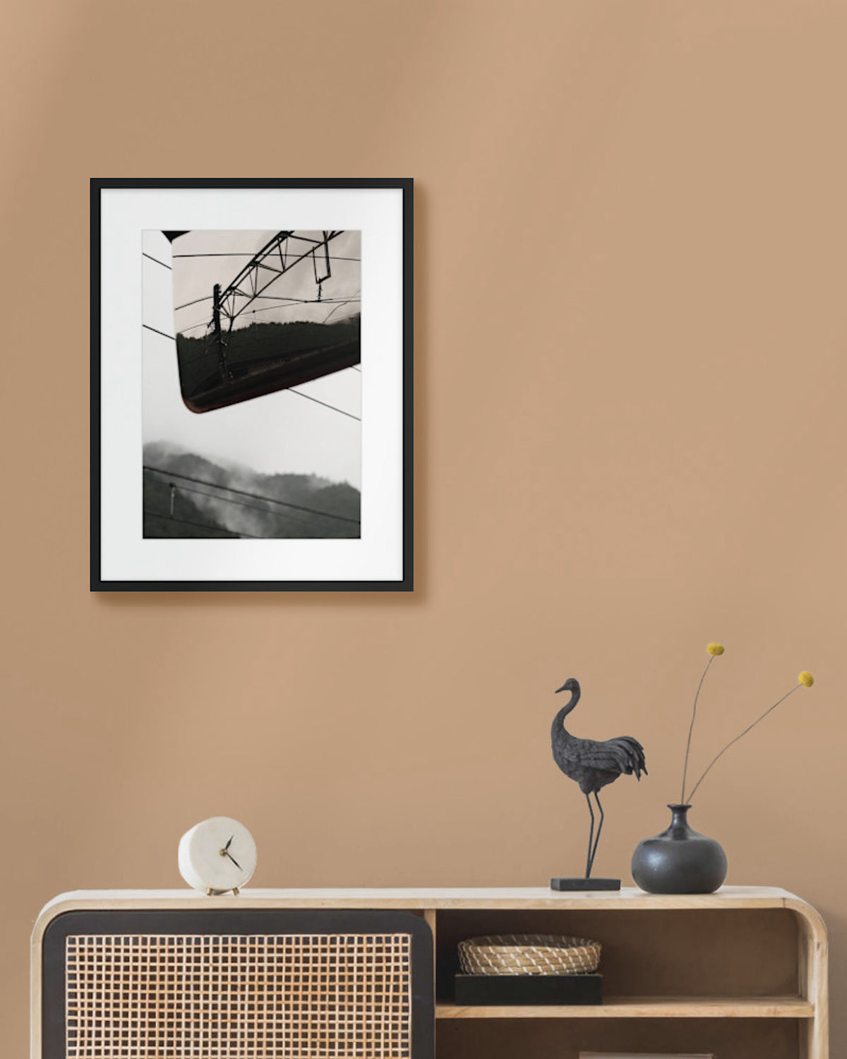 Framed mountain landscape photograph on a beige wall above a wooden console table with decorative items.