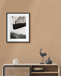 Framed mountain landscape photograph on a beige wall above a wooden console table with decorative items.