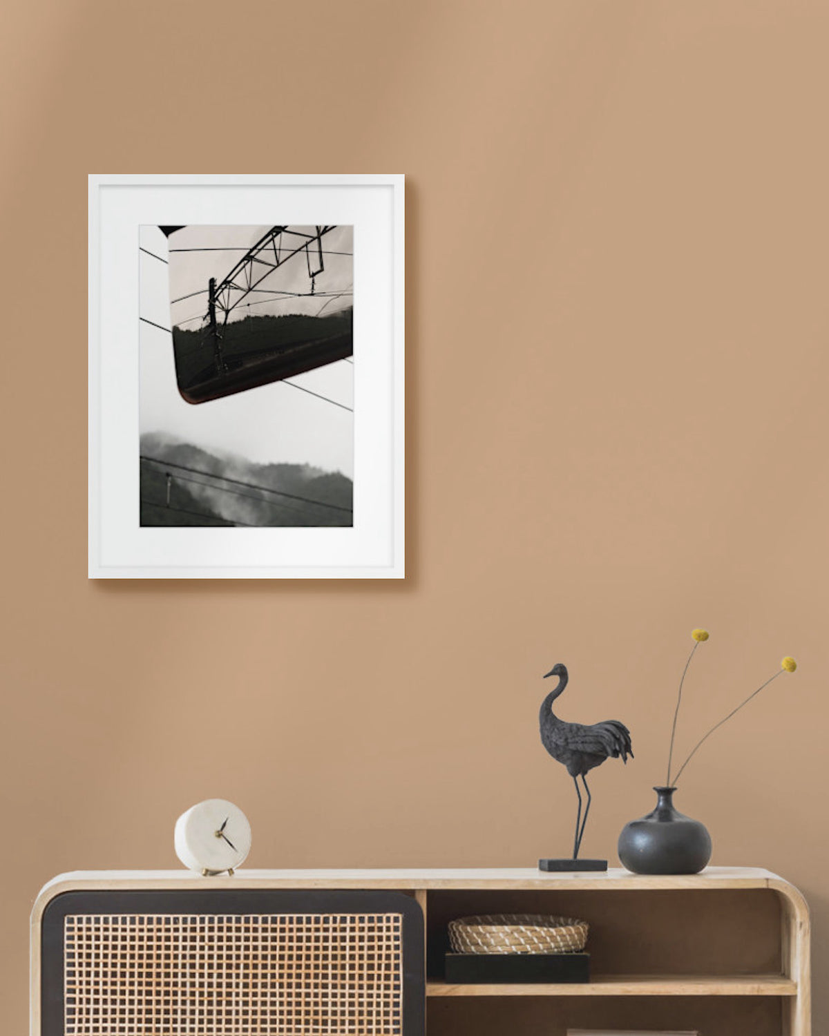 Framed landscape photograph on a beige wall above a wooden console table with decorative items.