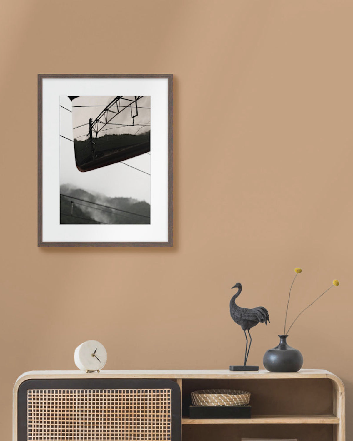 Framed landscape print on a beige wall above a wooden console table with decorative items.