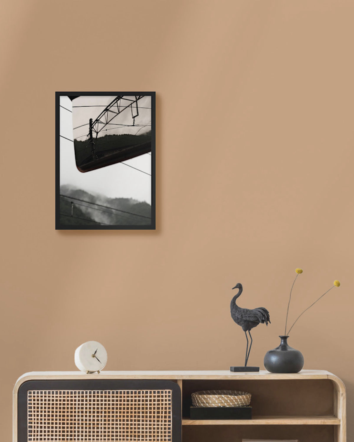 Framed landscape photograph
 on a beige wall above a wooden console table with decorative items.