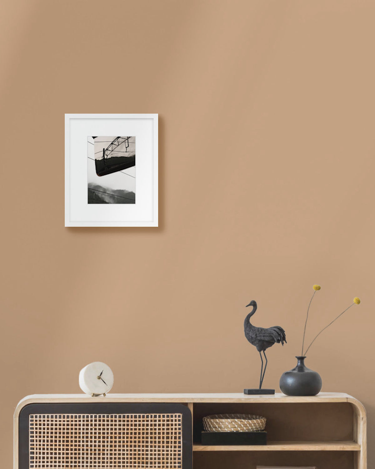 Framed japanese landscape photo on a beige wall above a wooden console table with decorative items.