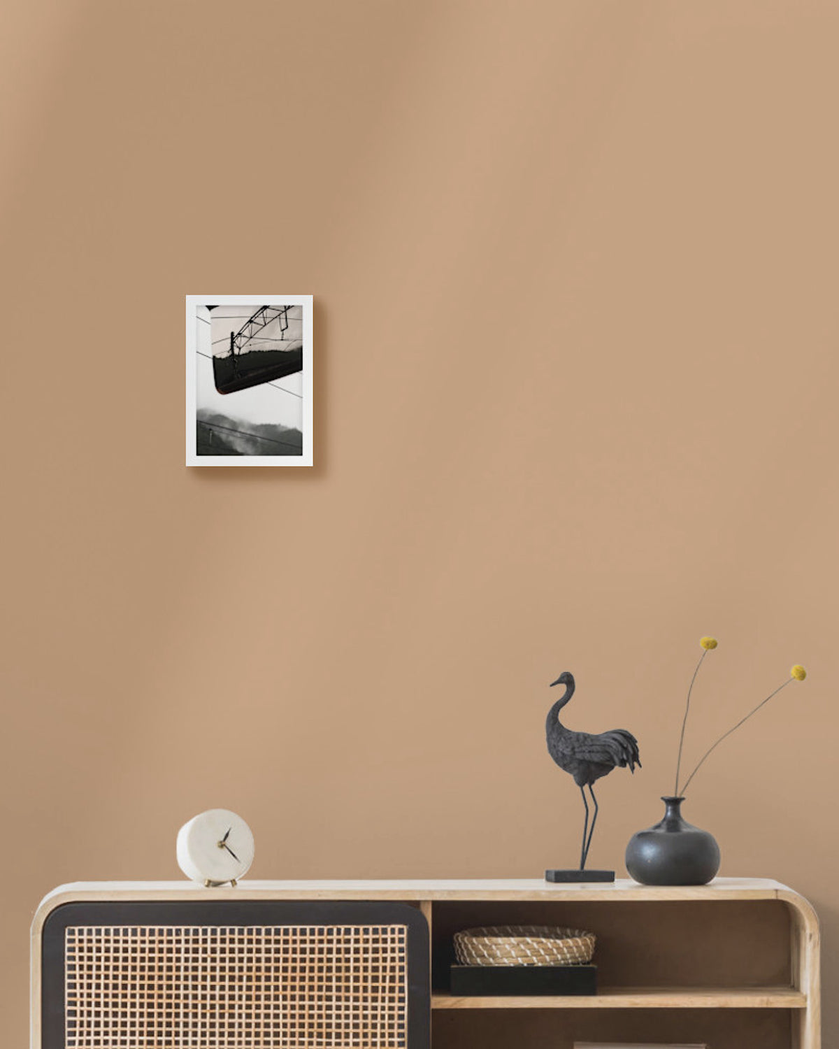 Framed landscape photo on a beige wall above a wooden console table with decorative items.