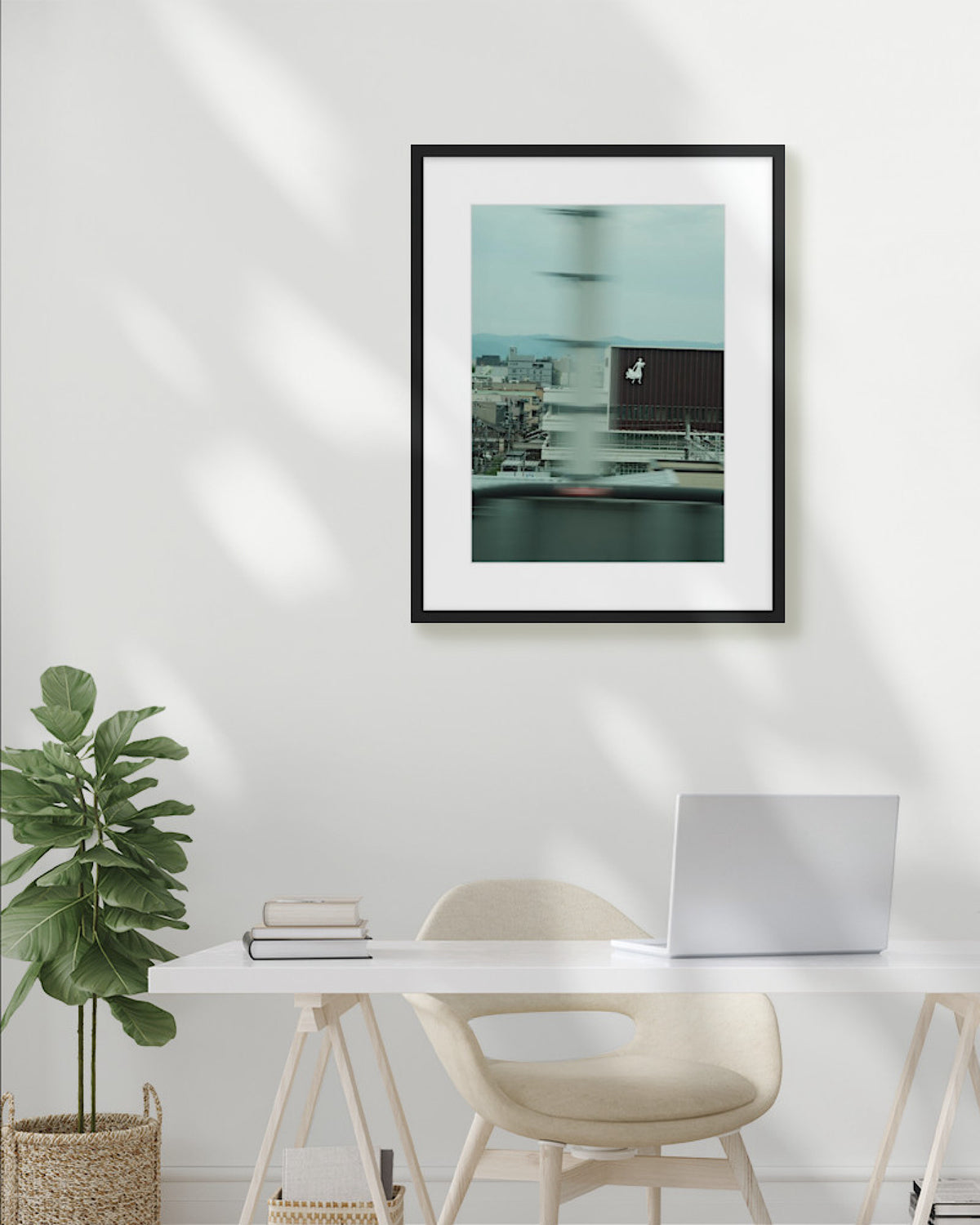 Framed photograph on a wall above a desk with a plant and laptop.