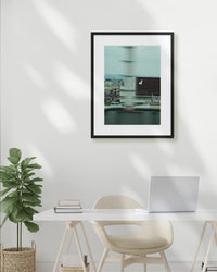 Framed photograph on a wall above a desk with a plant and laptop.