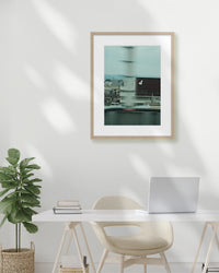 Framed artwork above a desk with a plant and laptop in a minimalistic room.