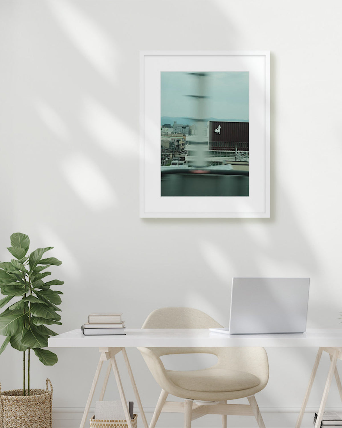 Framed artwork on a wall above a desk with a plant and laptop.