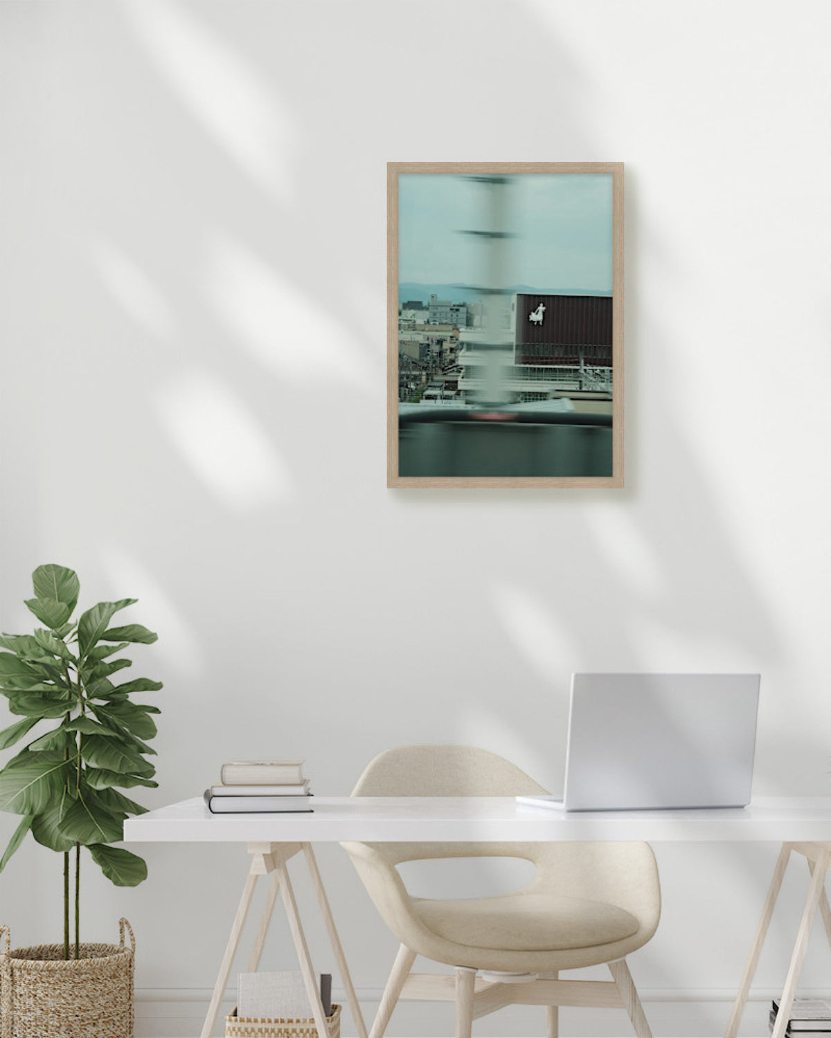 Modern office setup with a desk, chair, plant, and framed artwork on a white wall.