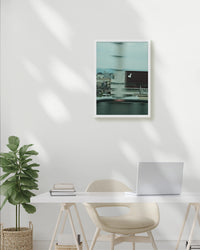 Modern office setup with a desk, chair, plant, and framed artwork on a white wall.