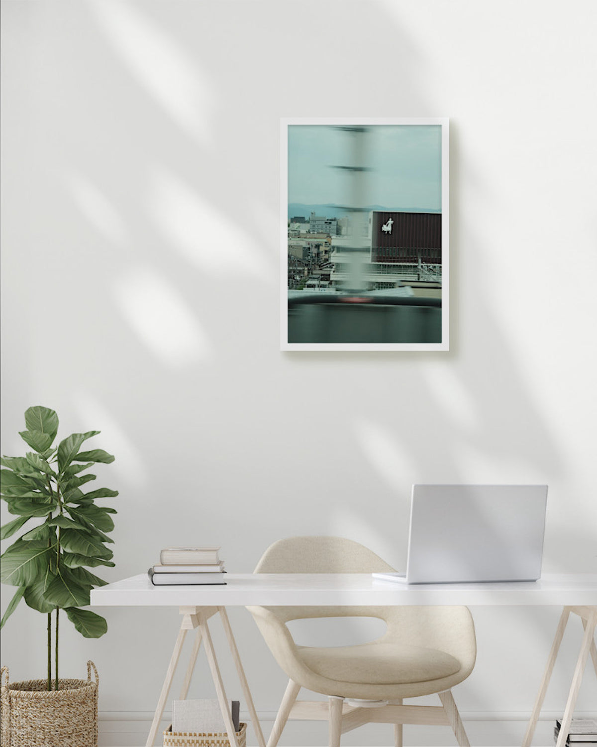 Modern office setup with a desk, chair, plant, and framed artwork on a white wall.